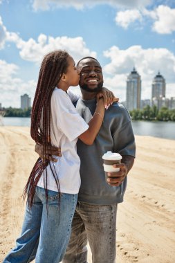 Sevgi dolu bir çift, güneşli bir günde suyun kenarında yürürken gülümser ve kucaklaşır..