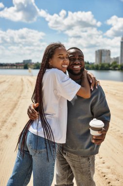 Sevgi dolu bir çift, nehir kenarında manzaralı bir yürüyüş yaparken birbirlerini mutlu bir şekilde kucaklarlar..