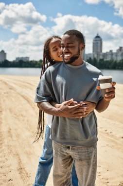 Sevgi dolu bir çift kumsalda birlikte gezer, günün tadını çıkarırken gülücüklerini ve içkilerini paylaşır..