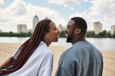 Birbirini seven çiftler nehir kenarında yürürler, mavi gökyüzünün altında gülücükler ve neşe paylaşırlar..