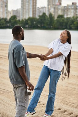 Nehir kenarında el ele gezen, sıcak güneş ışığında gülen neşeli bir çift..