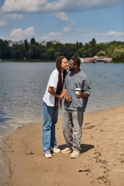 Sevgi dolu bir çift, güneşli bir öğleden sonra suyun kenarında yürürken neşeli bir anı paylaşır..