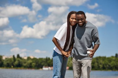 Genç bir çift su kenarında güzel bir yürüyüş yapar, gülümseyerek ve birbirlerini kucaklayarak..