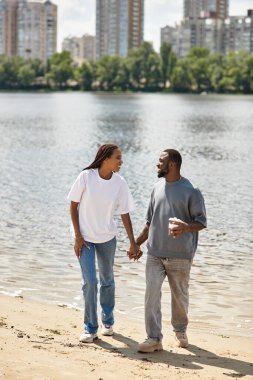 İki genç insan mutlu bir şekilde nehir kenarında el ele yürür, neşeli anları paylaşırlar..