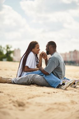 Genç çift sıcak kumda otururken, aşk ve kahkahaya dalmış bir anı paylaşıyor..