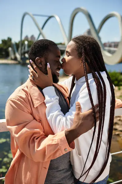 Neşeli genç çift, doğayla çevrili güneşli bir deniz yürüyüşü sırasında şefkatli bir öpücüğü paylaşıyor..