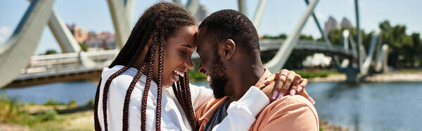 Молодая пара наслаждается романтической прогулкой вдоль берега реки, обнимаясь и улыбаясь друг другу.