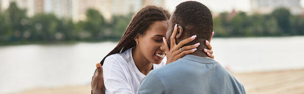 A loving couple embraces each other near the water, enjoying the warmth of the day and their bond.