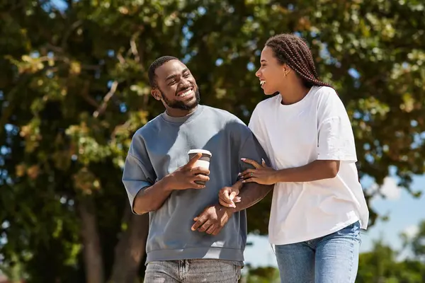 Sevgi dolu bir çift parktaki sıcak güneş ışığı altında el ele gezer, gülümsemelerini paylaşır..