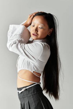 Genç bir kadın, modaya uygun kıyafetlerini ve parlak mavi saçlarını gri arka planda sergiliyor..