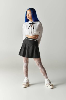 Şık, mavi saçlı, şık, genç bir kadın kendine güvenen gri bir stüdyo ortamında poz veriyor..