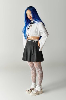 Gri bir stüdyoda modern moda akımlarını yakalayan genç bir kadın şık kıyafetini sunar..