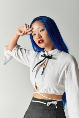 Genç Asyalı bir kadın kendine güvenerek şık bir kıyafet içinde poz veriyor, mavi saçlarını sergiliyor..