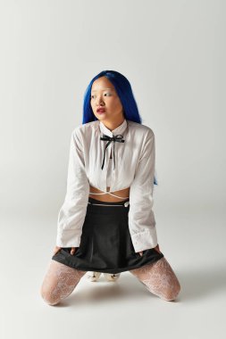 Canlı mavi saçlı Asyalı genç bir kadın şık kıyafetini minimalist bir stüdyoda sunar..