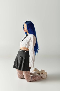 Çarpıcı mavi saçlı güzel genç bir kadın modern gri bir stüdyoda zarifçe poz veriyor..