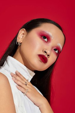 Genç bir Asyalı kadın, eşsiz stilini ve göz makyajını koyu kırmızı arka planda gösteriyor..
