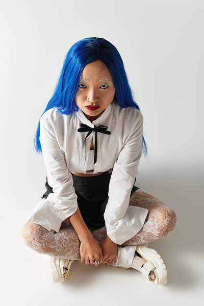Молодая азиатка демонстрирует свой модный наряд и голубые волосы в стильной студии.