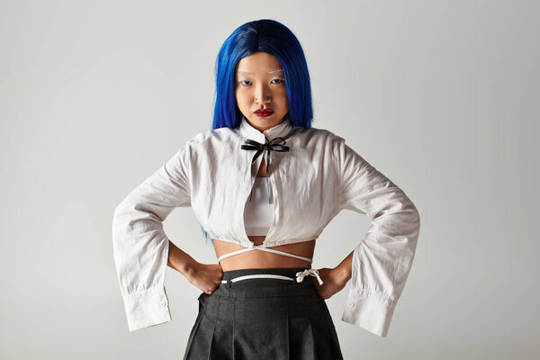 A young woman with blue hair models a stylish outfit in a modern studio, exuding confidence.