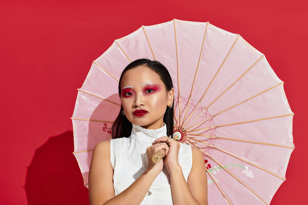 Молодая азиатка демонстрирует свой яркий макияж и зонтик на ярком красном фоне..