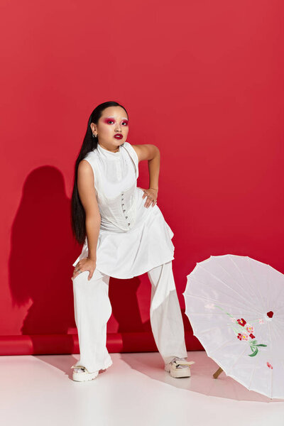 Молодая азиатка излучает уверенность в стильном наряде, позируя в современной красной студии.