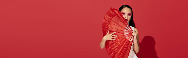 A stylish young asian woman displays her creativity with striking eye makeup while posing with a fan, banner