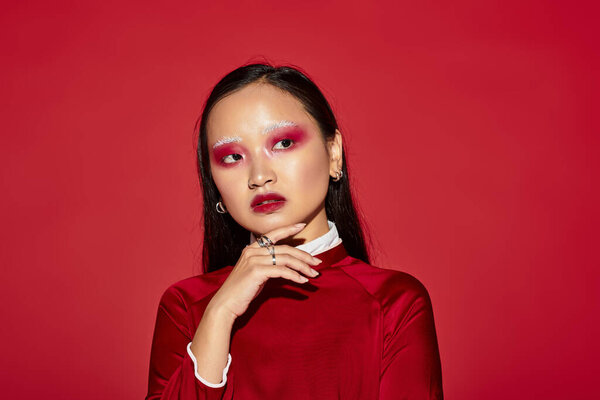 Молодая азиатка элегантно позирует в красной студии, демонстрируя яркий макияж и модную моду..