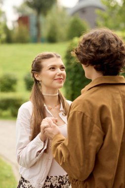 Birbirini seven çiftler, huzurlu bir parkta yürürken birbirlerine tatlı bakışlar atıyorlar.