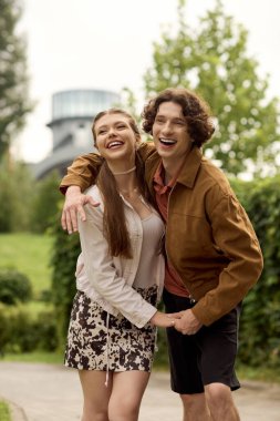 Genç bir çift, ağaçlarla çevrili verimli bir parkta romantik bir yürüyüş yaparken ışıl ışıl gülümsüyor..