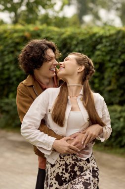 Genç çift, doğa yürüyüşü sırasında birbirlerine sıcak bir şekilde sarılır, gülümsemelerini ve sevgilerini paylaşır..