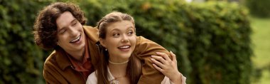 Neşeli genç bir çift, yemyeşil bir parkta el ele gezer, kahkahalar ve sevgiyi paylaşır..