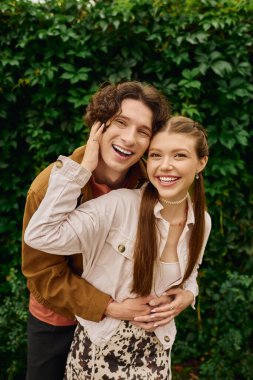 İki aşık mutlu bir anı paylaşır, el ele yürürler, yemyeşil park manzarasıyla çevrili..