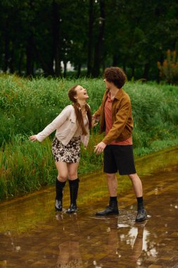 İki genç yetişkin parkta yürüyor, gülüyor ve yağmurlu bir günün keyfini kucaklıyor..