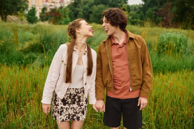 Genç çift gülüyor ve romantik bir parkta el ele yürüyor..