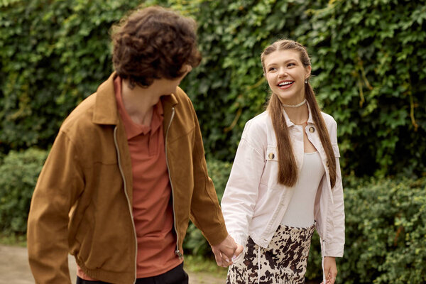 A young couple walks hand in hand, sharing smiles and laughter surrounded by nature.