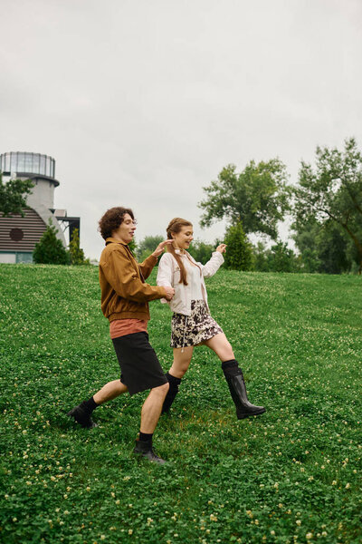 Молодая пара разделяет смех, когда они идут рука об руку через пышный зеленый парк настройки.