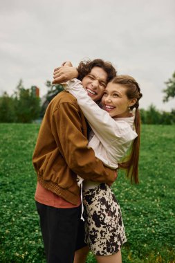 Genç bir çift, yemyeşil bir parkta el ele gülüşmeler ve kahkahalar atarak yürüyor..