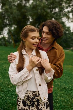 Genç çift yemyeşil bir parkta el ele dolaşır, sevgi ve mutluluk saçar..