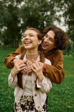 Genç bir çift yemyeşil bir parkta gezer, gülücükler ve güneşin altında bağlantı anlarını paylaşır..