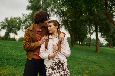 Bir erkek, bir kadının alnından nazikçe öper... yemyeşil bir parkta mutlu bir uyum içinde yürürken..