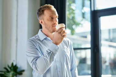 Genç bir profesyonel, şık bir ofiste çalışırken kahvesinden zevk alır..