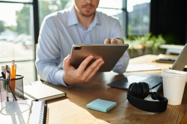 Genç adam masasındaki görevlere tablet kullanarak odaklandı ve ofis gereksinimleriyle çevrildi..