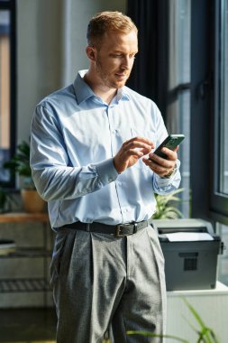Genç profesyonel, üretkenliği vurgulamak için şık bir ofiste akıllı telefon kullanıyor..