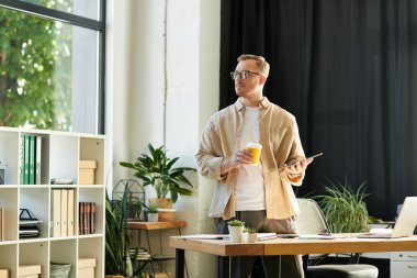 Genç ve şık bir profesyonel, parlak yeşil bir ofiste tablet ve kahve kullanır..