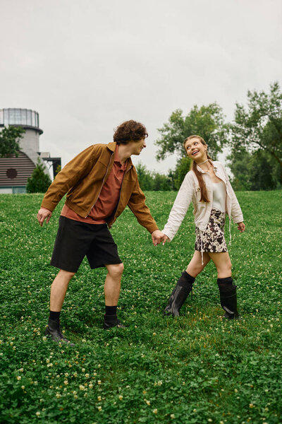 A young couple shares a romantic stroll hand in hand through a lush park.