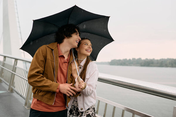 Young lovers stroll hand in hand beneath an umbrella, embracing joy amidst a light rain.