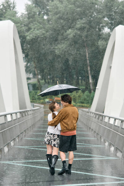 Young couple enjoys a romantic stroll in the rain, sharing joy and warmth beneath an umbrella.