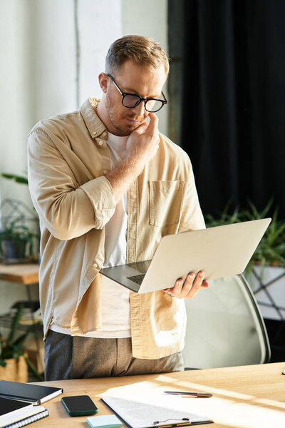 Молодой предприниматель рассматривает бизнес-решения в современном рабочем пространстве, с ноутбуком в руке.