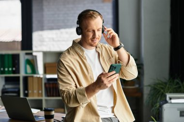 Ofiste yakışıklı bir genç adam akıllı telefonu üzerinde çalışırken müzik dinliyor..