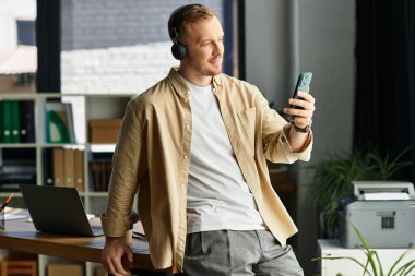 Masada oturan genç bir profesyonel, parlak bir ofiste akıllı telefonunun keyfini çıkarır..