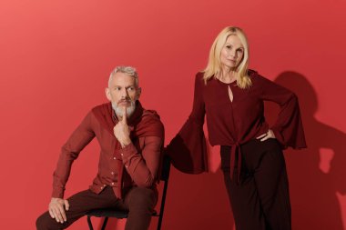 Şık ve sevecen bir son sınıf çifti cesur, kırmızı bir arka plana karşı birlikte poz verir..